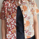 Person wearing a floral patterned shirt over a black dress against a plain background