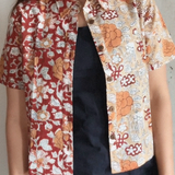 Person wearing a floral patterned shirt over a black dress against a plain background