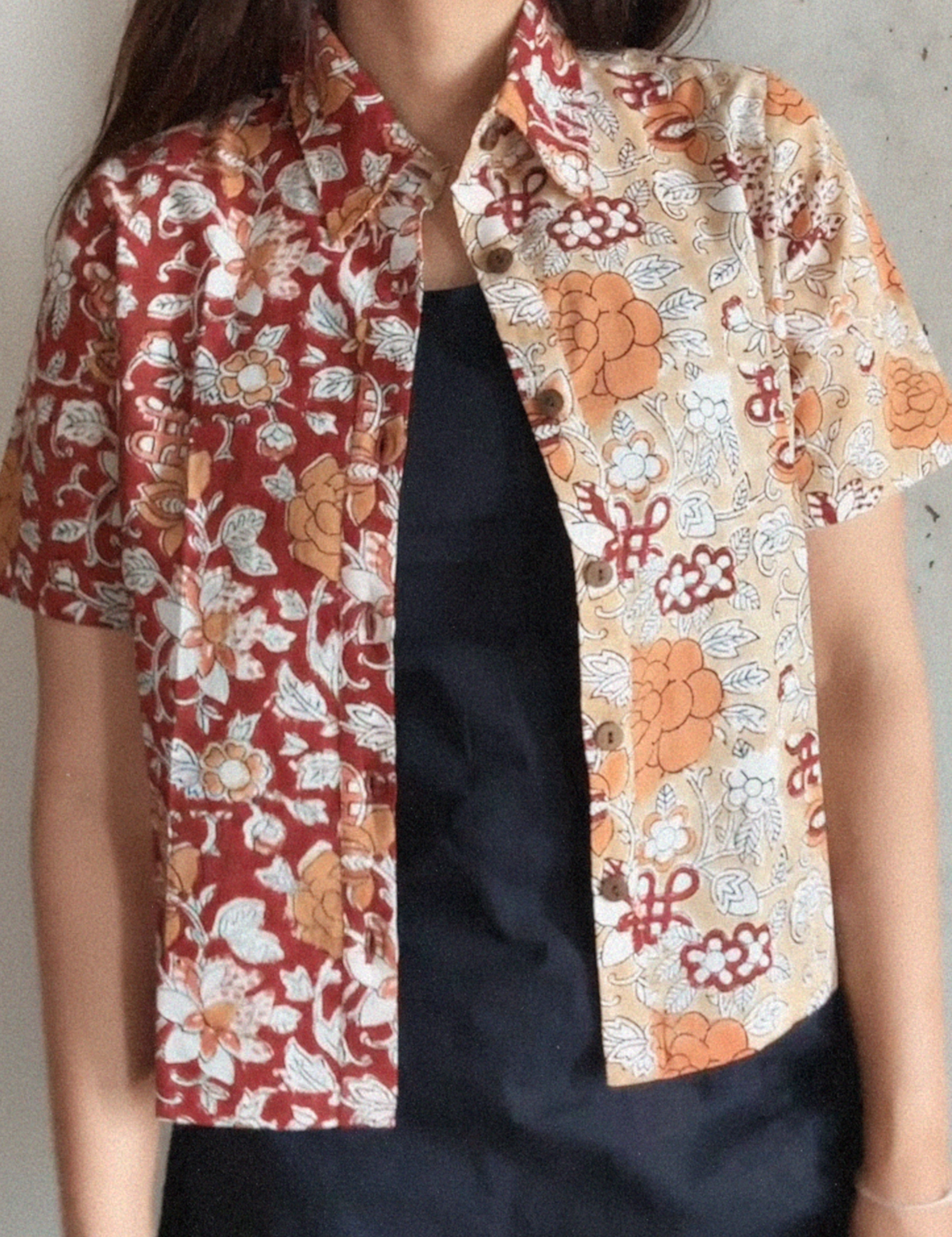 Person wearing a floral patterned shirt over a black dress against a plain background