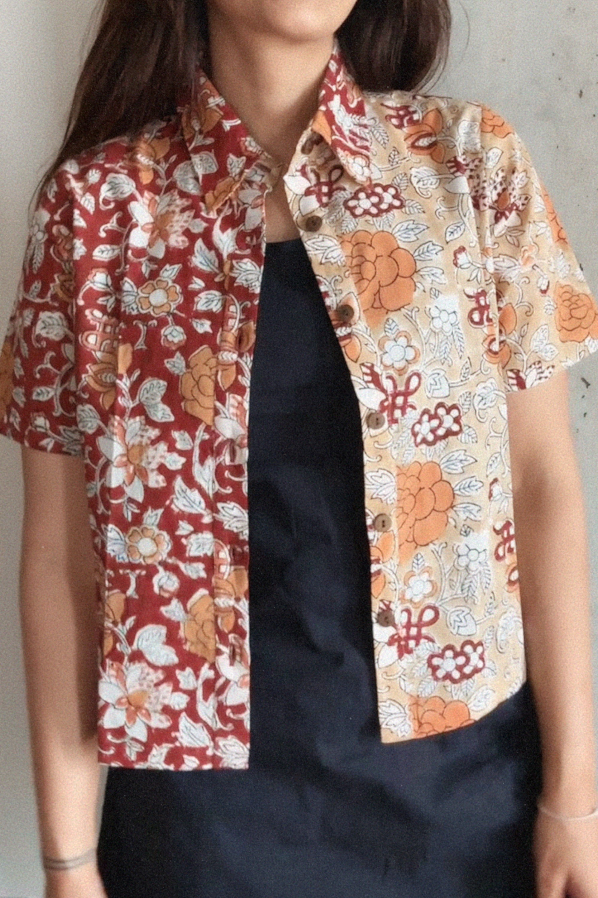 Person wearing a floral patterned shirt over a black dress against a plain background