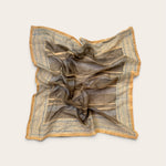 A square scarf with a brown and beige striped pattern and blue geometric border details, styled in a loose crumpled shape on a light beige background.