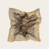 A square scarf with a brown and beige striped pattern and blue geometric border details, styled in a loose crumpled shape on a light beige background.