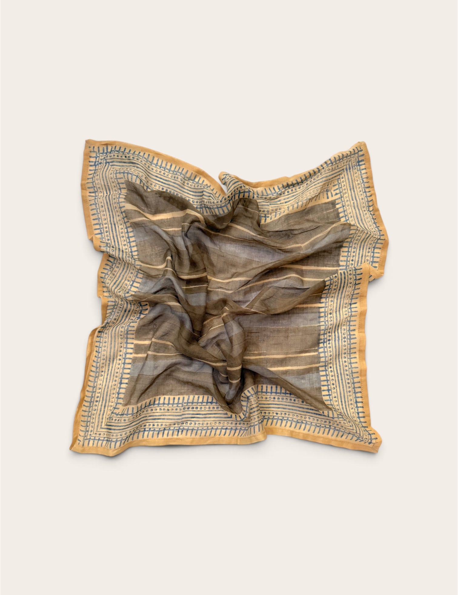 A square scarf with a brown and beige striped pattern and blue geometric border details, styled in a loose crumpled shape on a light beige background.
