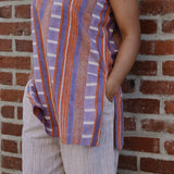 Person wearing a sleeveless red and purple striped top and pant set, standing against a brick wall. Close up on side pant pocket. 