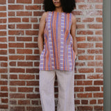 Woman wearing a red and purple striped sleeveless top and wide-leg pants standing against a brick wall.