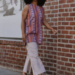 Woman in a red and purple striped sleeveless top and pants walking by a brick wall.