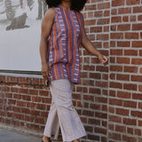 Woman in a red and purple striped sleeveless top and pants walking by a brick wall.