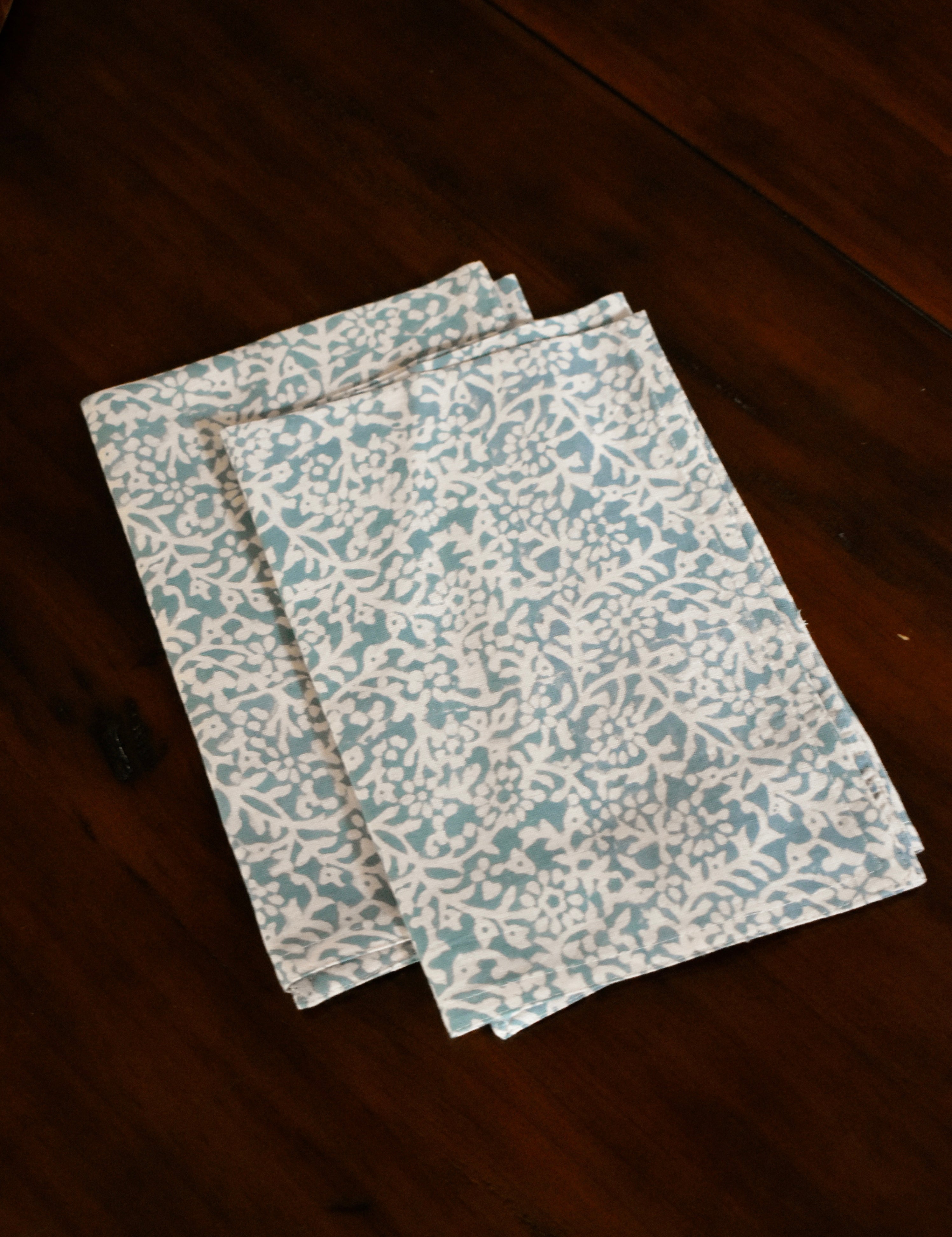 Two blue floral printed table napkins folded on wooden table
