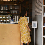 Woman in a yellow floral midi dress standing at a counter in a store.