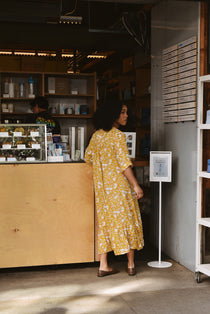 Woman in a yellow floral midi dress standing at a counter in a store.