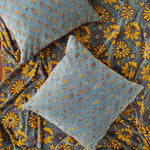 Two floral printed velvet pillows laid flat on top of yellow floral printed velvet blanket.