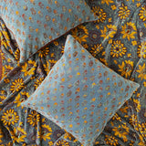 Two floral printed velvet pillows laid flat on top of yellow floral printed velvet blanket.