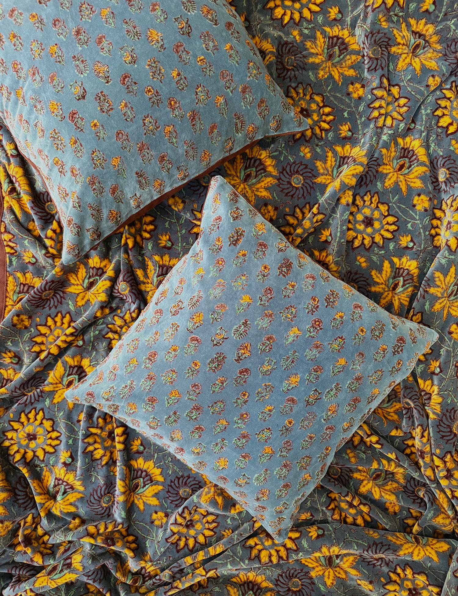 Two floral printed velvet pillows laid flat on top of yellow floral printed velvet blanket.