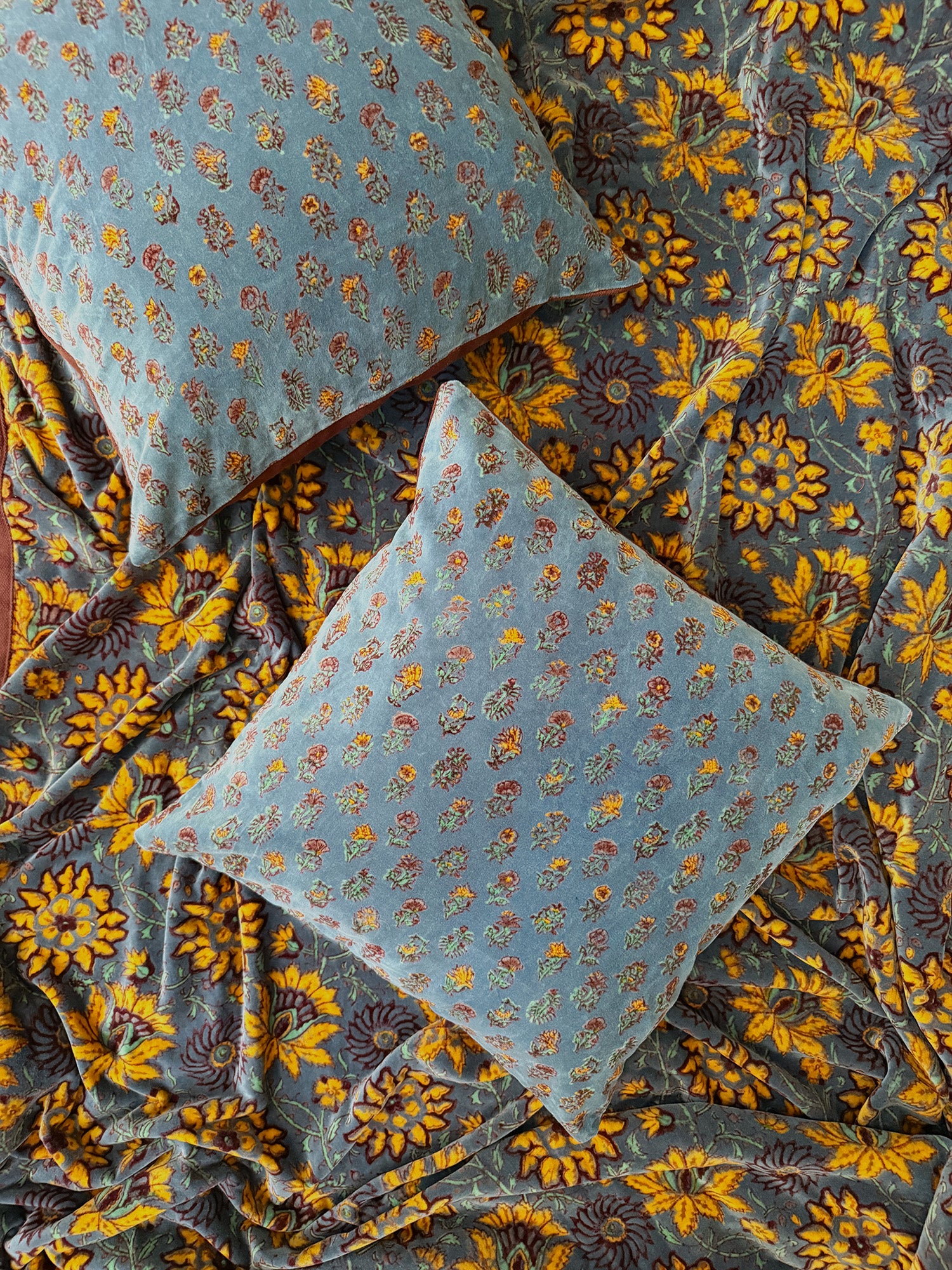 Two floral printed velvet pillows laid flat on top of yellow floral printed velvet blanket.
