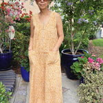Woman wearing sleeveless yellow cotton jumpsuit near flowers and trees outside
