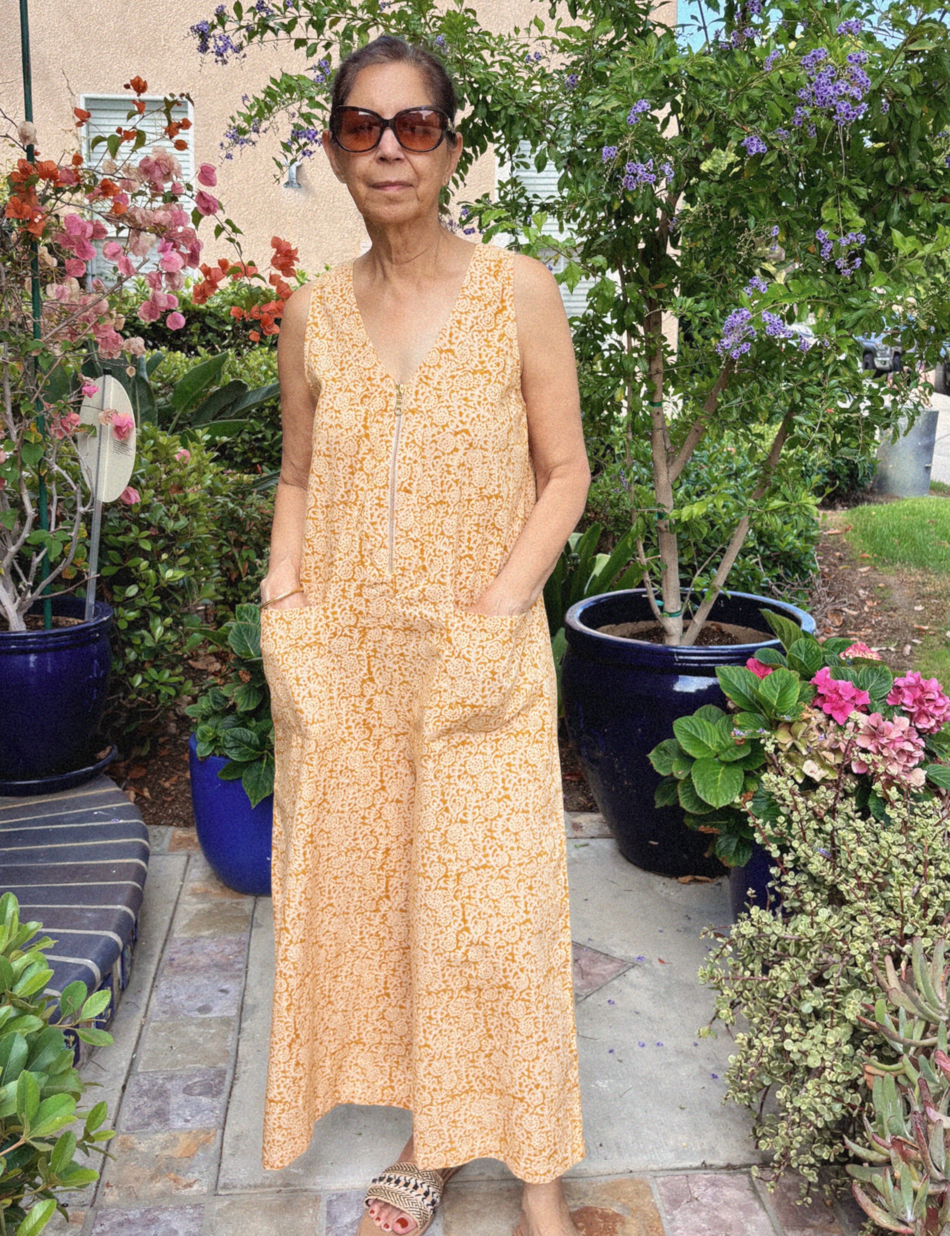 Woman wearing sleeveless yellow cotton jumpsuit near flowers and trees outside