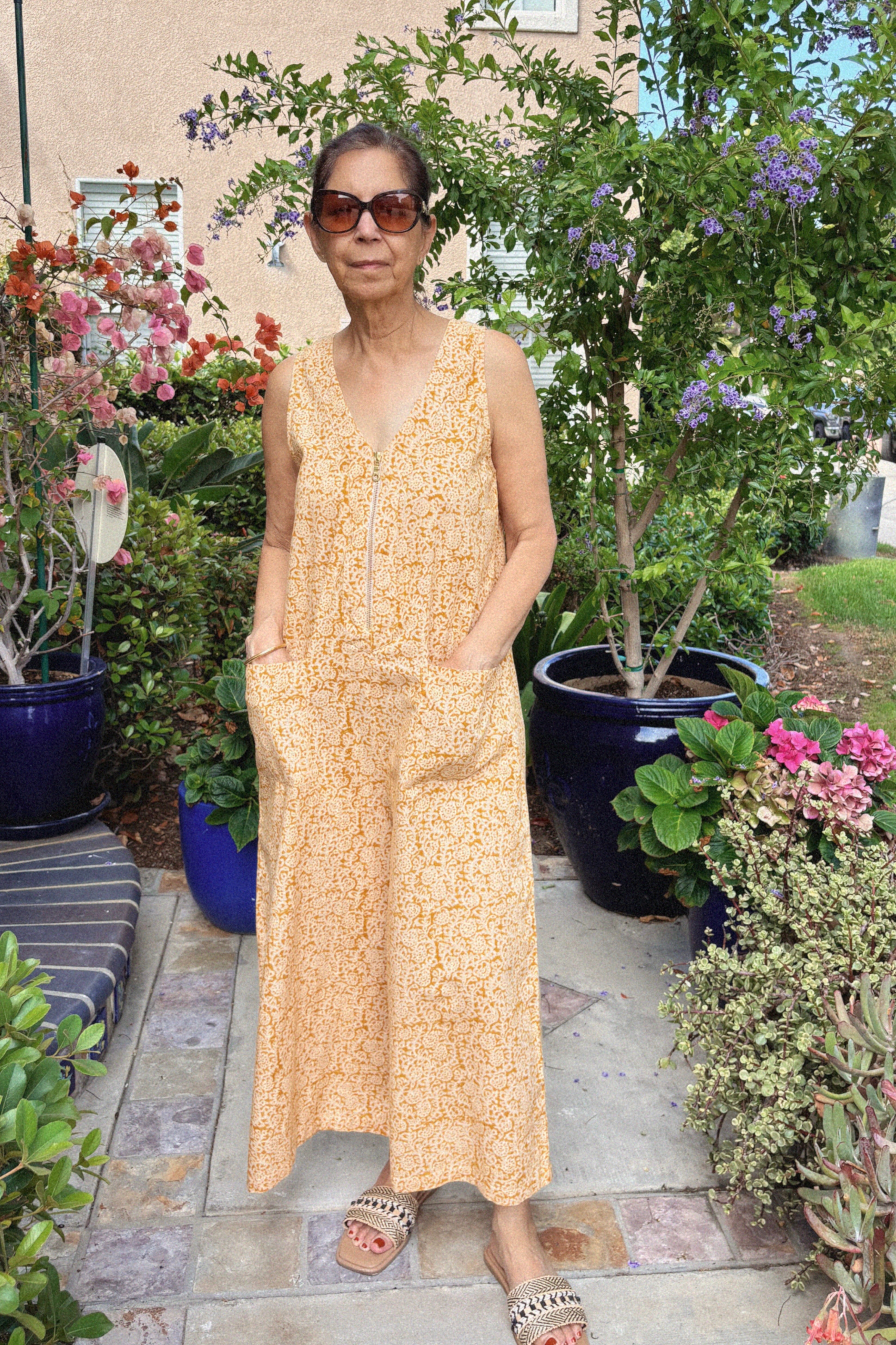 Woman wearing sleeveless yellow cotton jumpsuit near flowers and trees outside