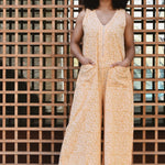 Woman standing against a grid-patterned surface with a building in the background, wearing a yellow floral print jumpsuit