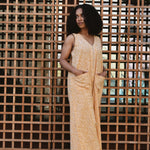 Woman in a yellow floral print jumpsuit standing in front of a grid patterned wall.