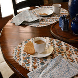 tablescape with floral printed placemats and napkins on a wooden table, with teacups, plates and biscuits