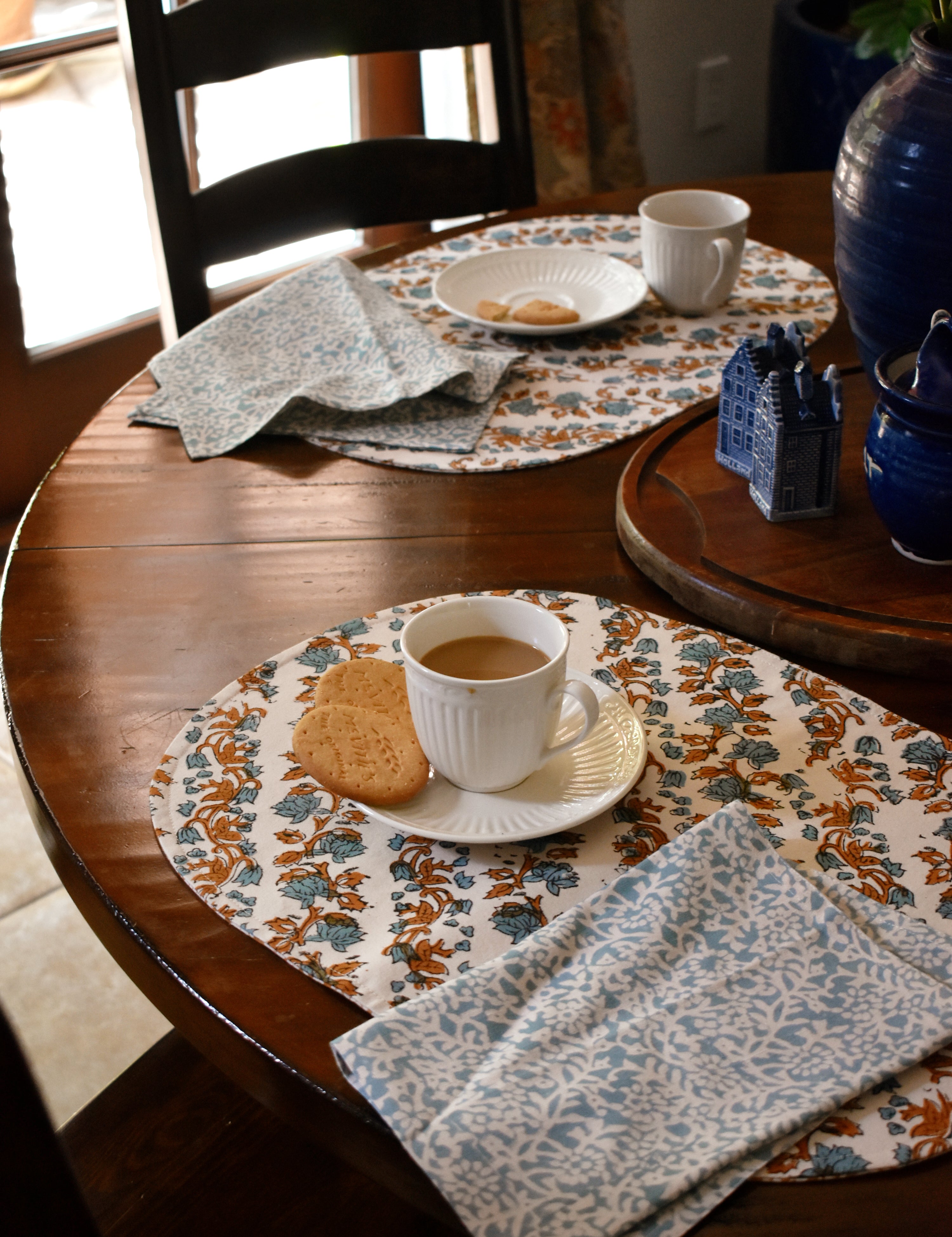 tablescape with floral printed placemats and napkins on a wooden table, with teacups, plates and biscuits