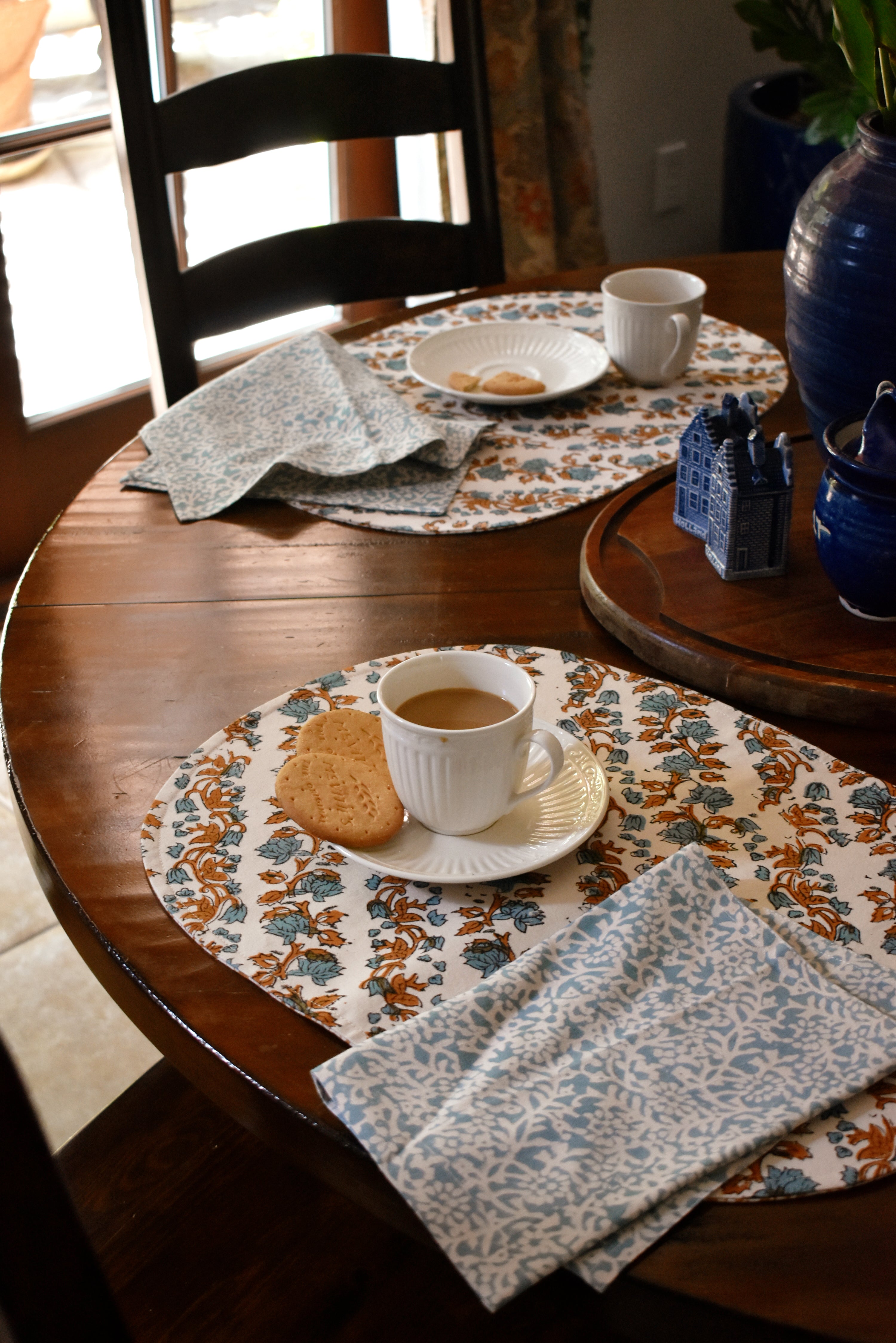 tablescape with floral printed placemats and napkins on a wooden table, with teacups, plates and biscuits