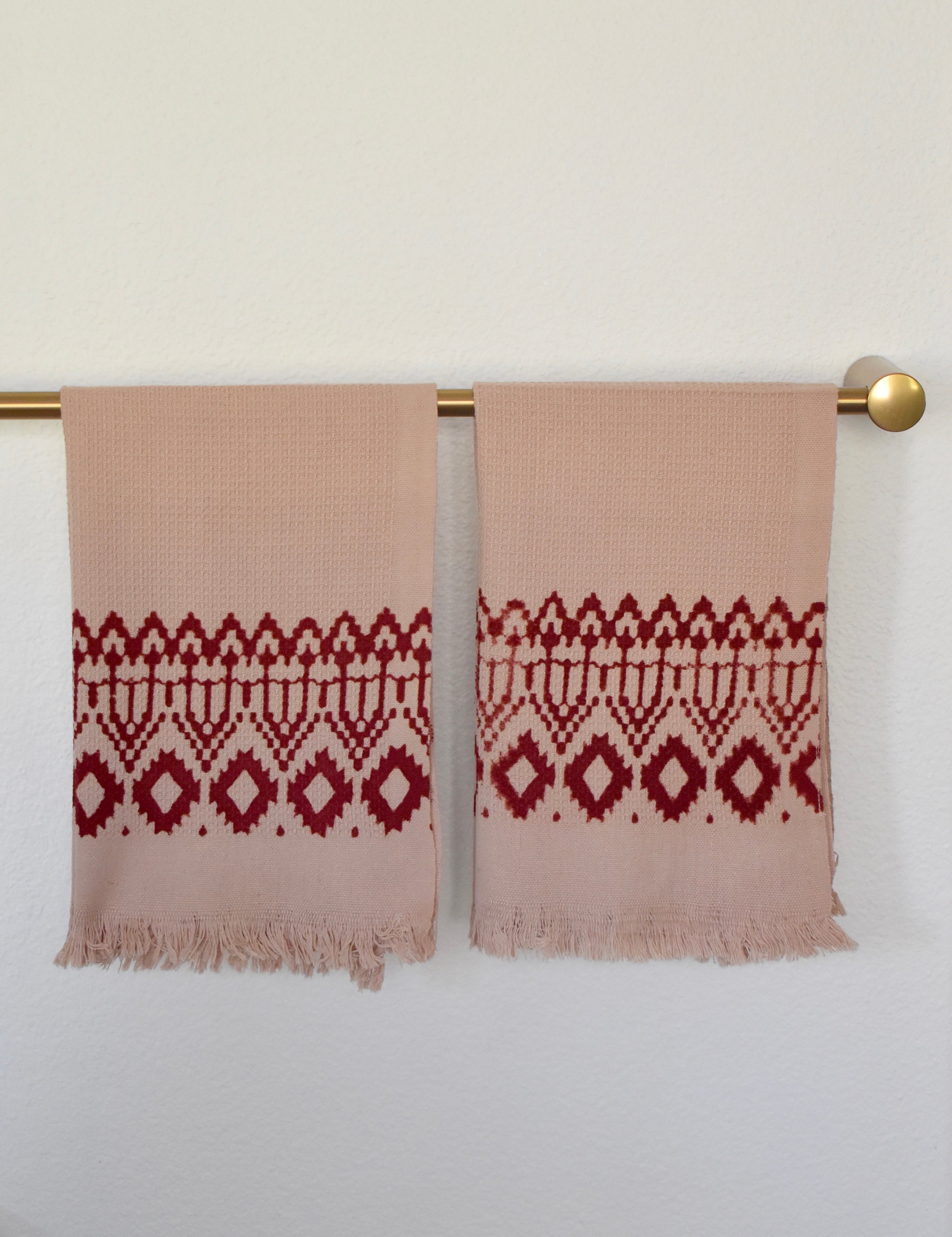 Block printed Terracotta hand towels, hanging on a golden rod. Towels have a geometric, diamond print. 