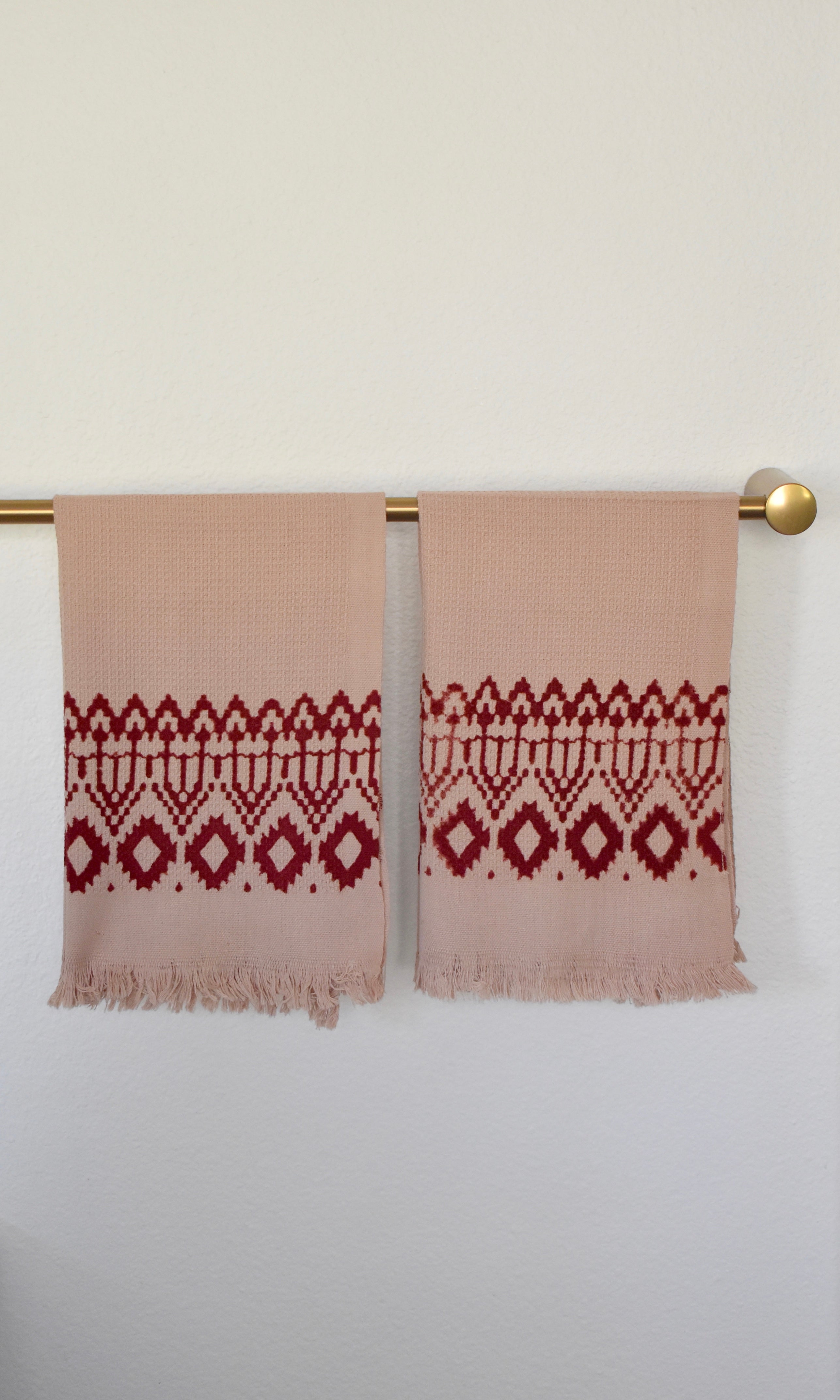 Block printed Terracotta hand towels, hanging on a golden rod. Towels have a geometric, diamond print. 