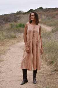 Model wearing sleeveless, cropped jumpsuit outside with heeled brown boots. Jumpsuit has rust floral print, two front pockets and front zipper.