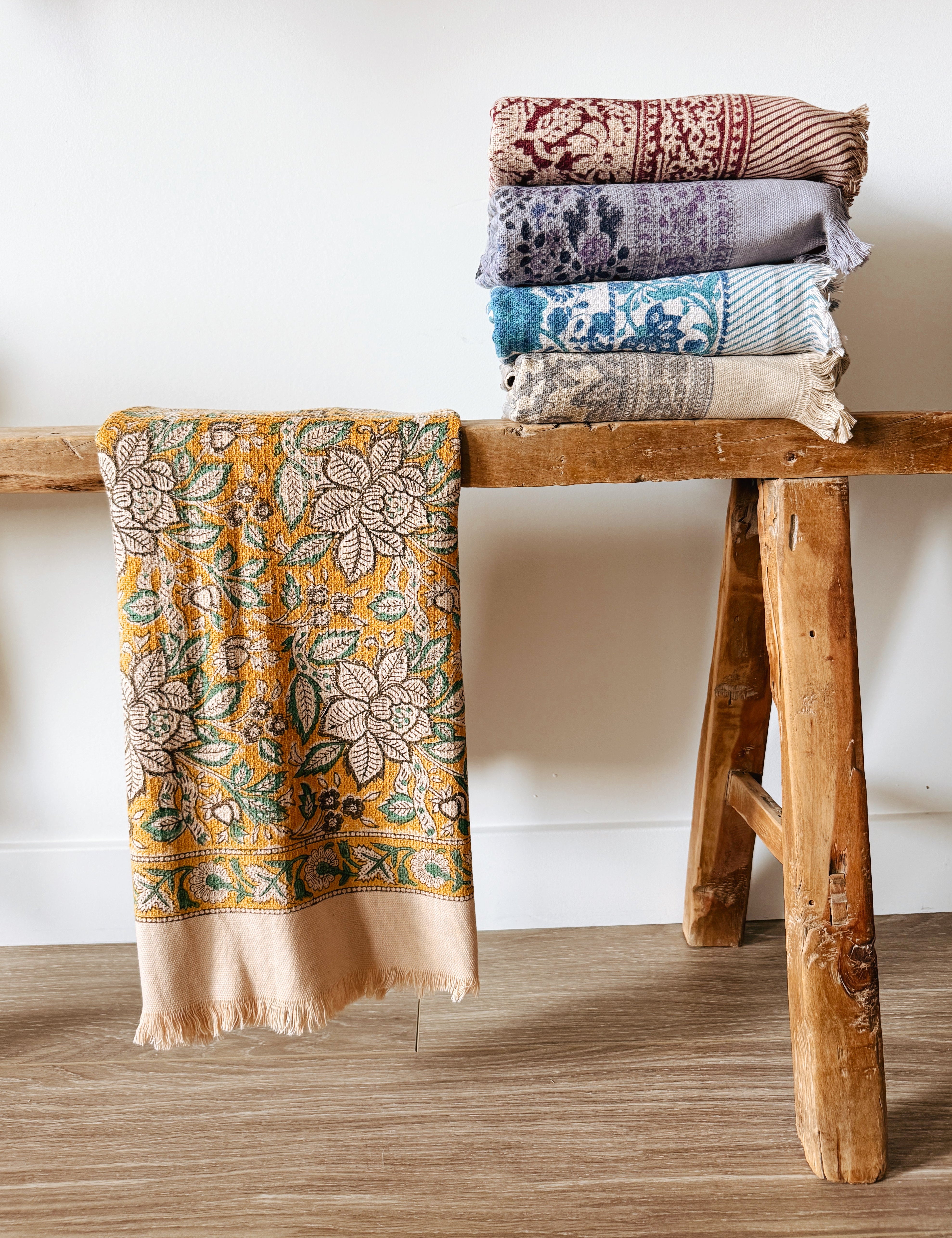 Stack of patterned bath towels on a wooden stool against a white wall