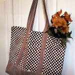 Checkered tote bag with striped handles hanging on a white door with flowers hanging out of the bag