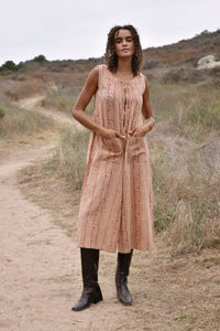 Model wearing sleeveless, cropped jumpsuit outside with heeled brown boots. Jumpsuit has rust floral print, two front pockets and front zipper. 