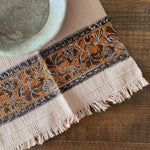 Decorative tablecloth with orange and brown floral pattern on a wooden surface
