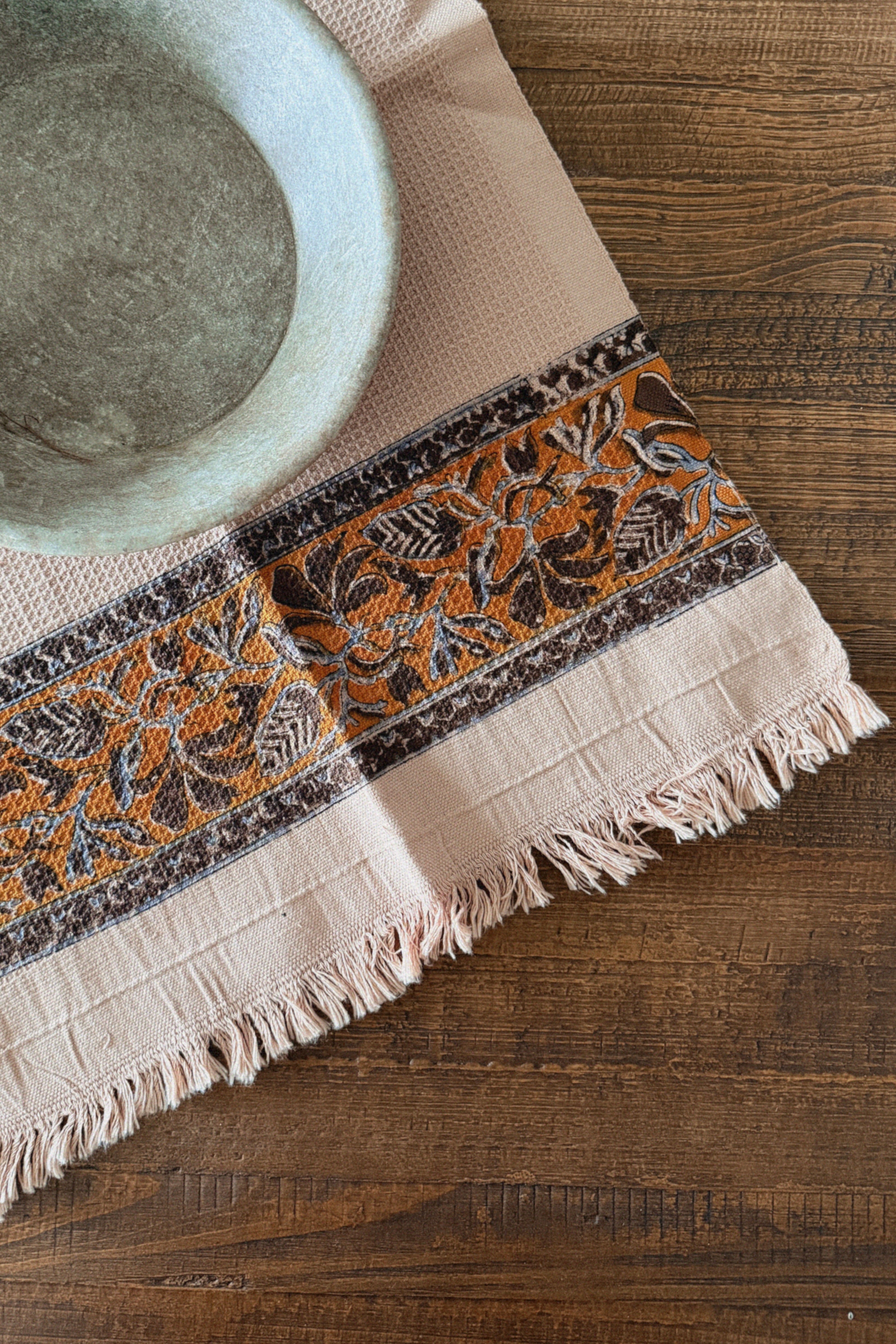 Decorative tablecloth with orange and brown floral pattern on a wooden surface