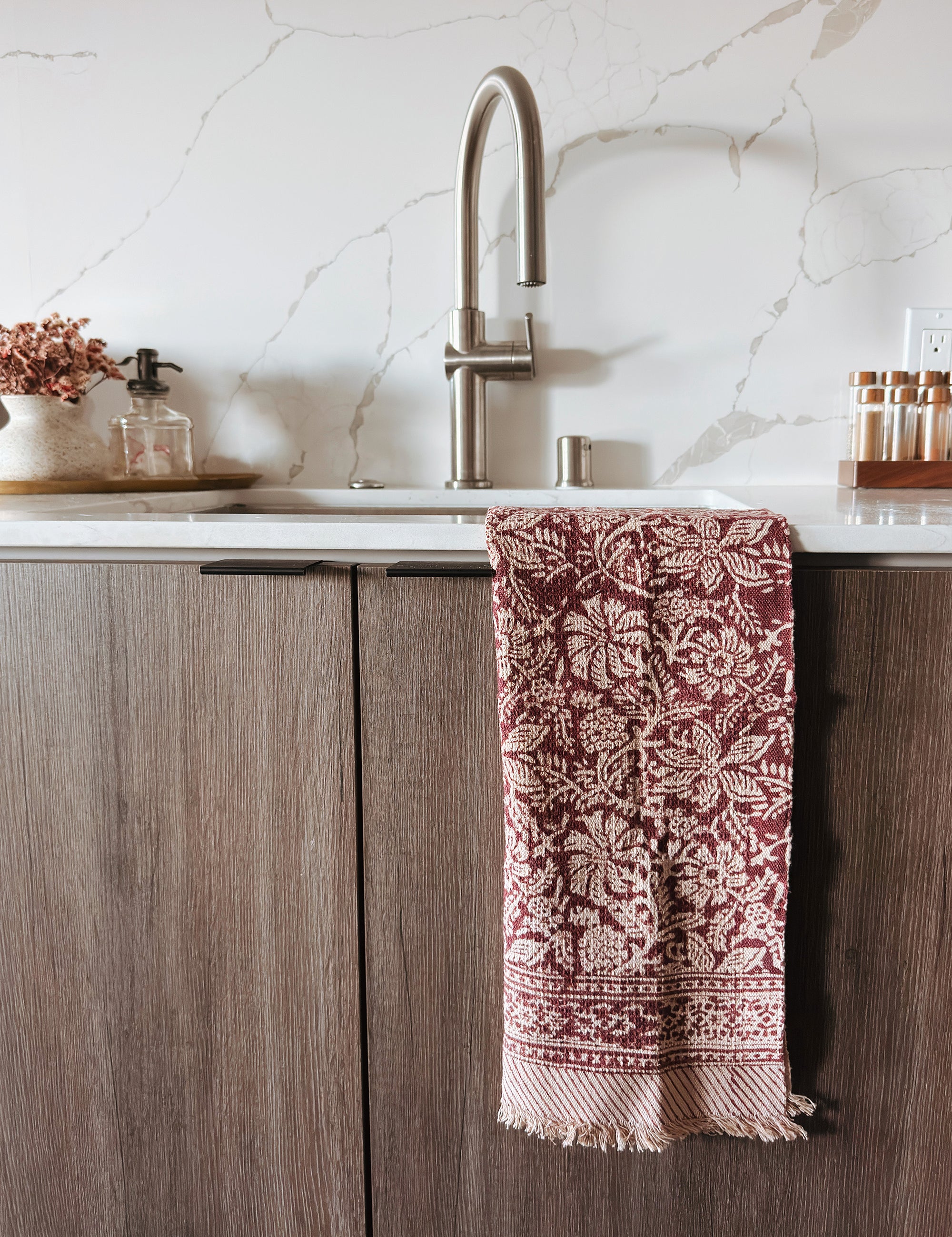 Kitchen with wooden cabinets, marble backsplash, and a patterned red and white towel hanging on the handle.