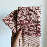 Hand holding two red floral patterned towels against a light background