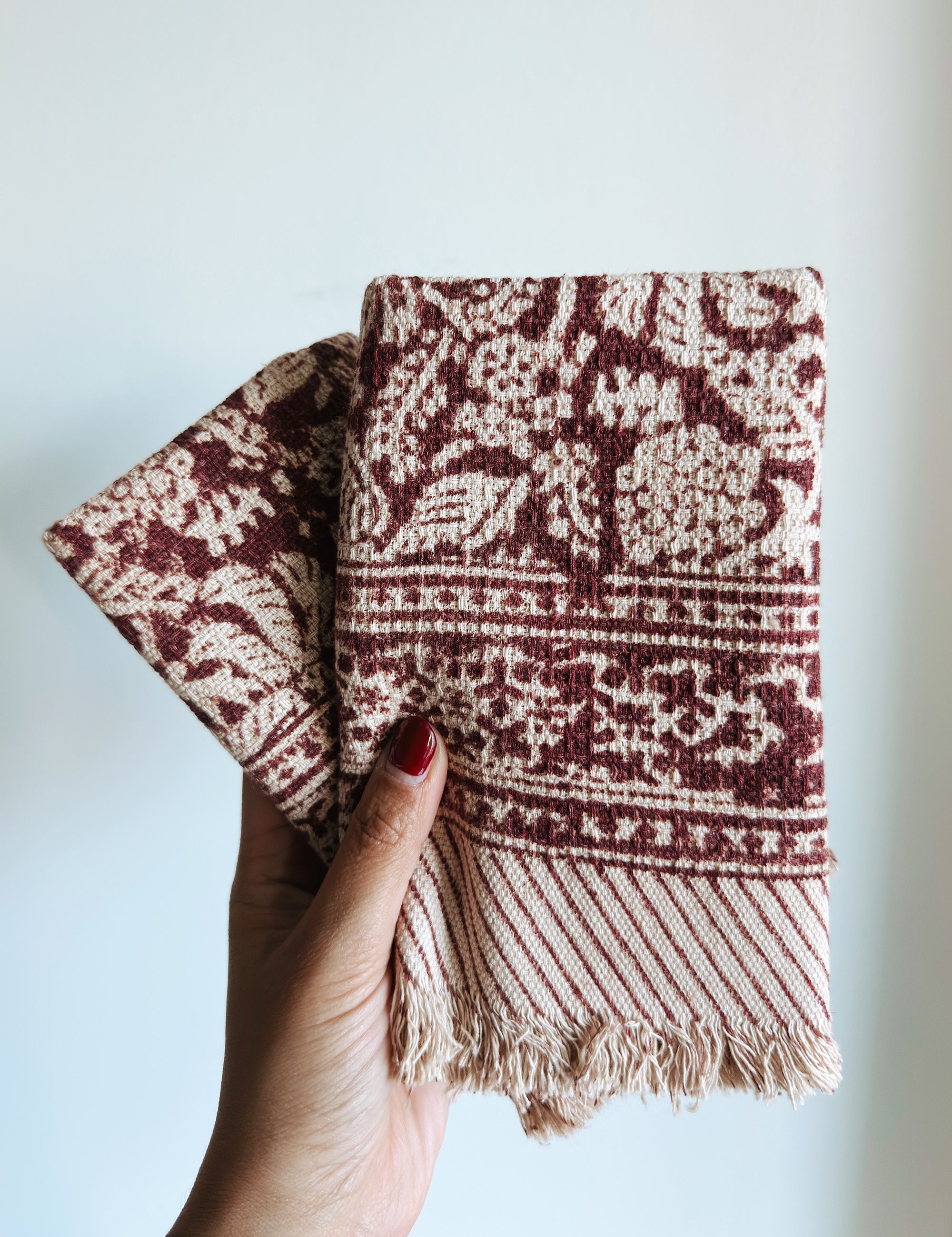 Hand holding two red floral patterned towels against a light background