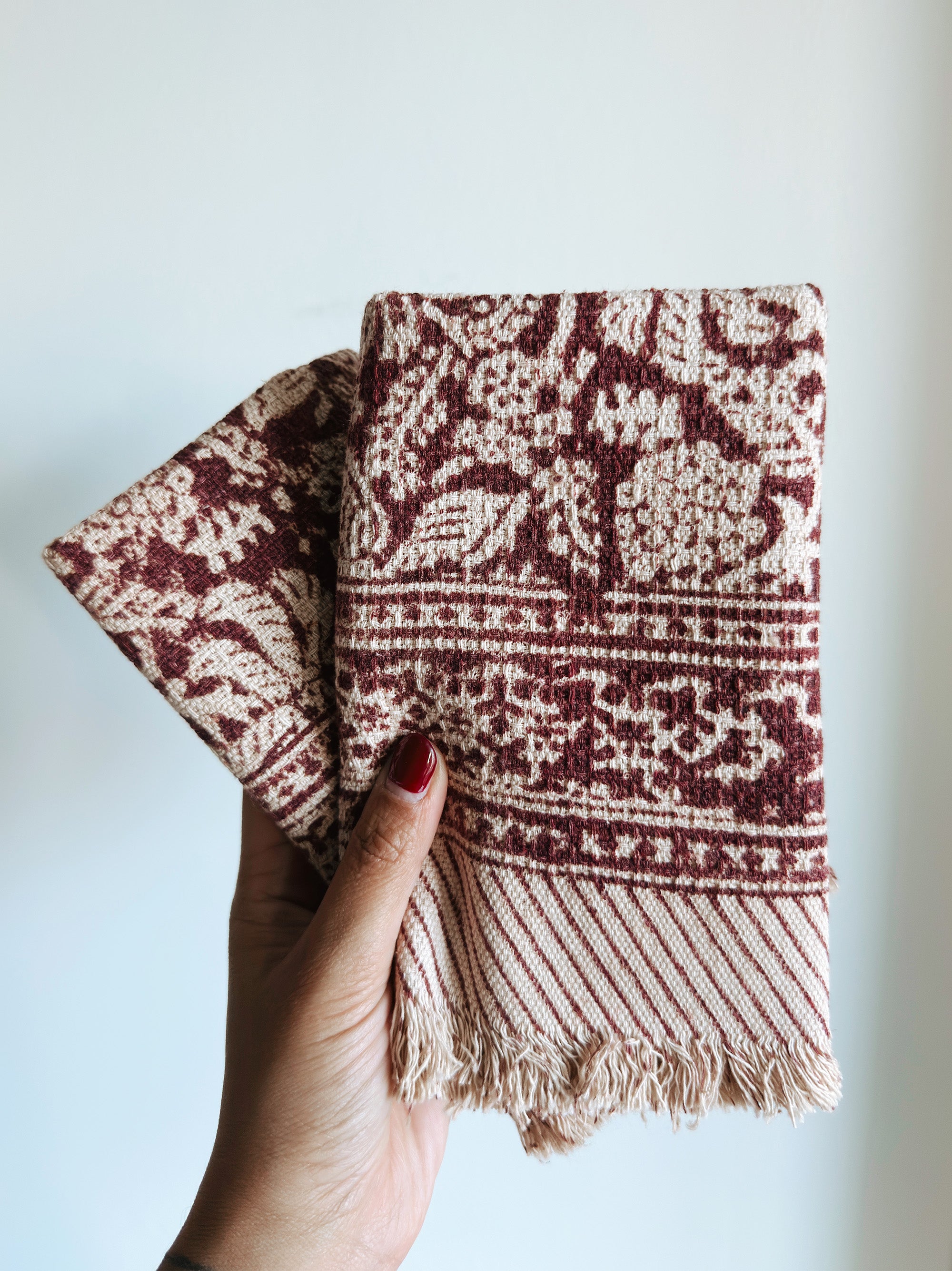Hand holding two red floral patterned towels against a light background