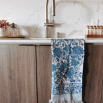 Blue and white patterned towel hanging on a wooden cabinet with a marble backsplash.