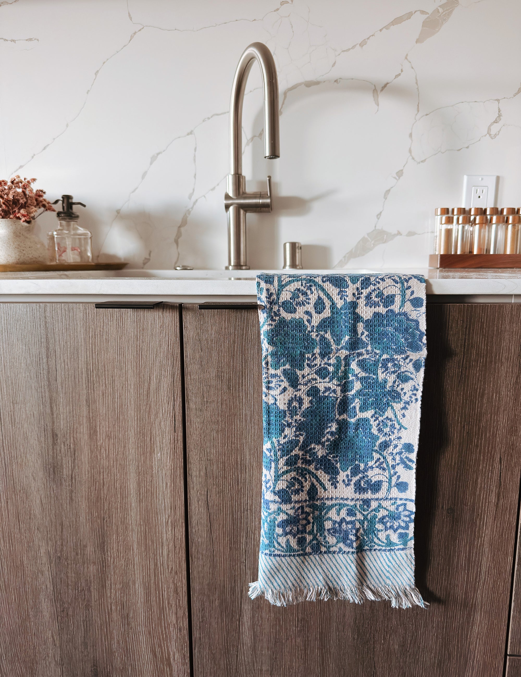 Blue and white patterned towel hanging on a wooden cabinet with a marble backsplash.