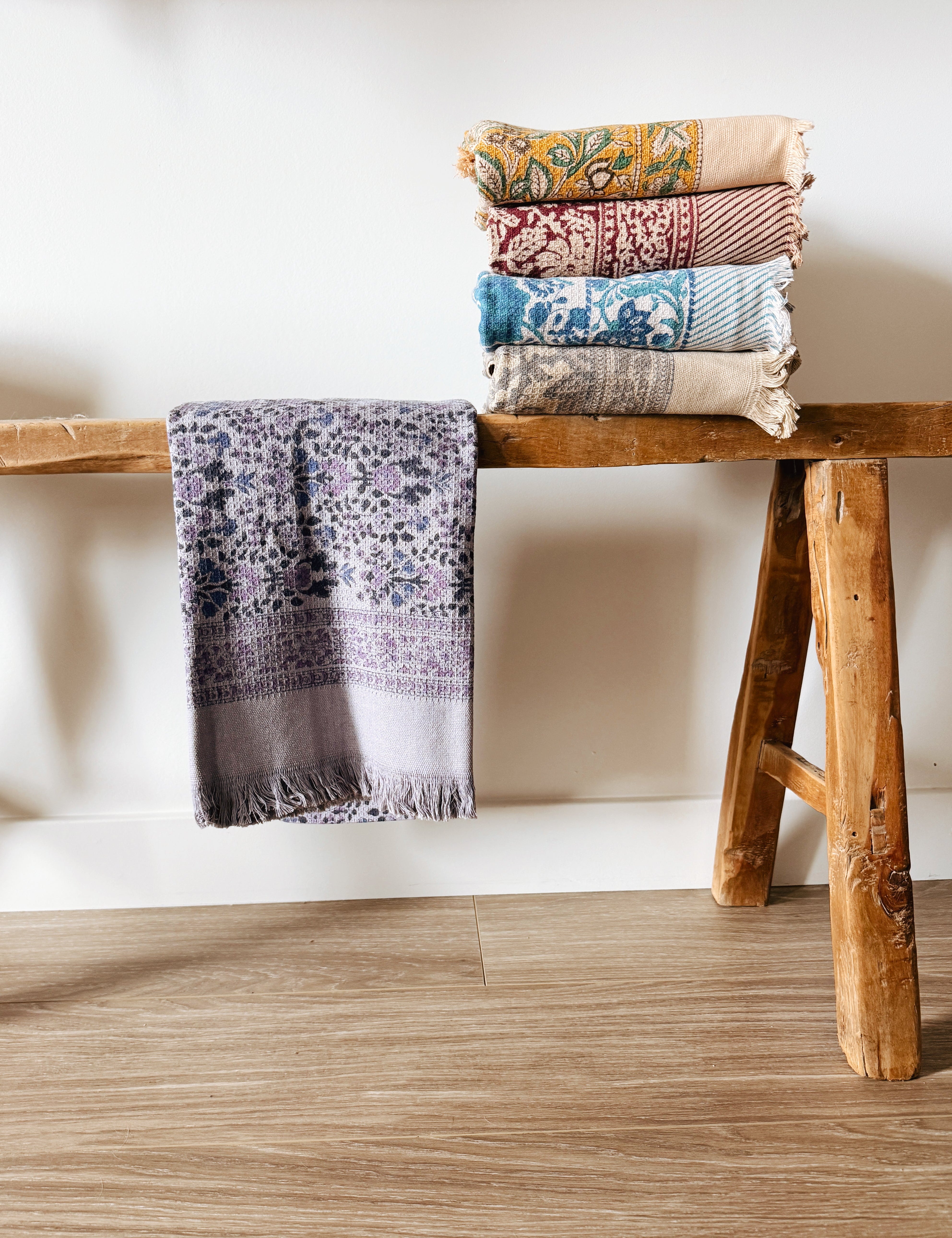 Stack of patterned towels on a wooden stool against a white wall.