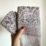 Hand holding folded purple floral-patterned hand towels against a plain background