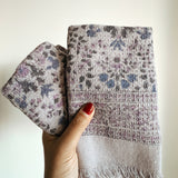 Hand holding folded purple floral-patterned hand towels against a plain background