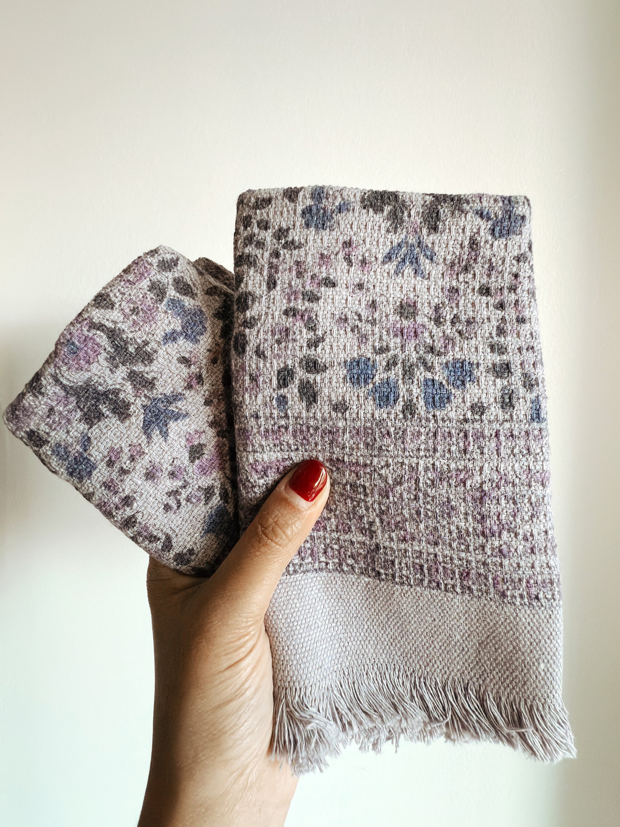 Hand holding folded purple floral-patterned hand towels against a plain background