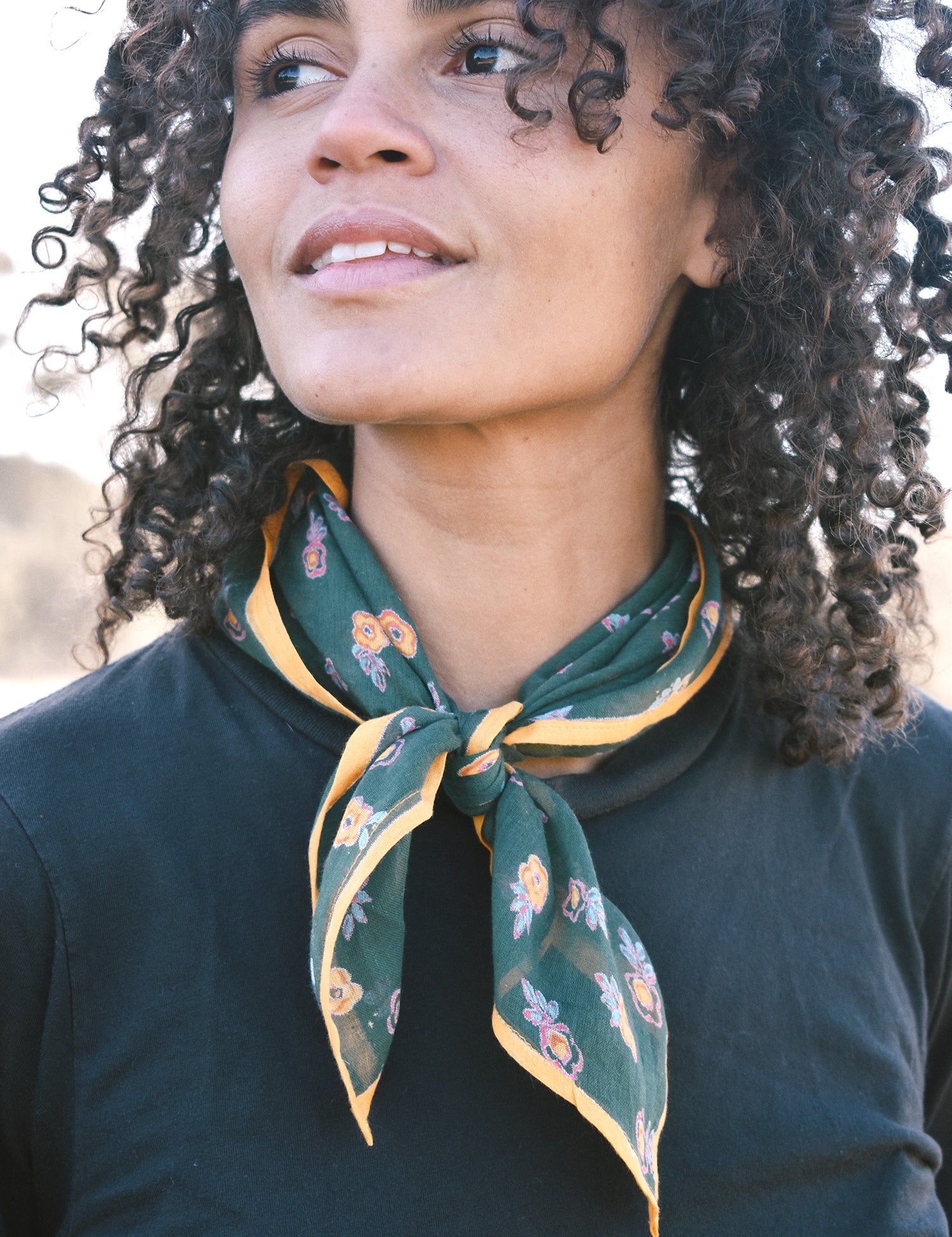 Woman wearing block print Calie bandana tied around neck against a black tee shirt.