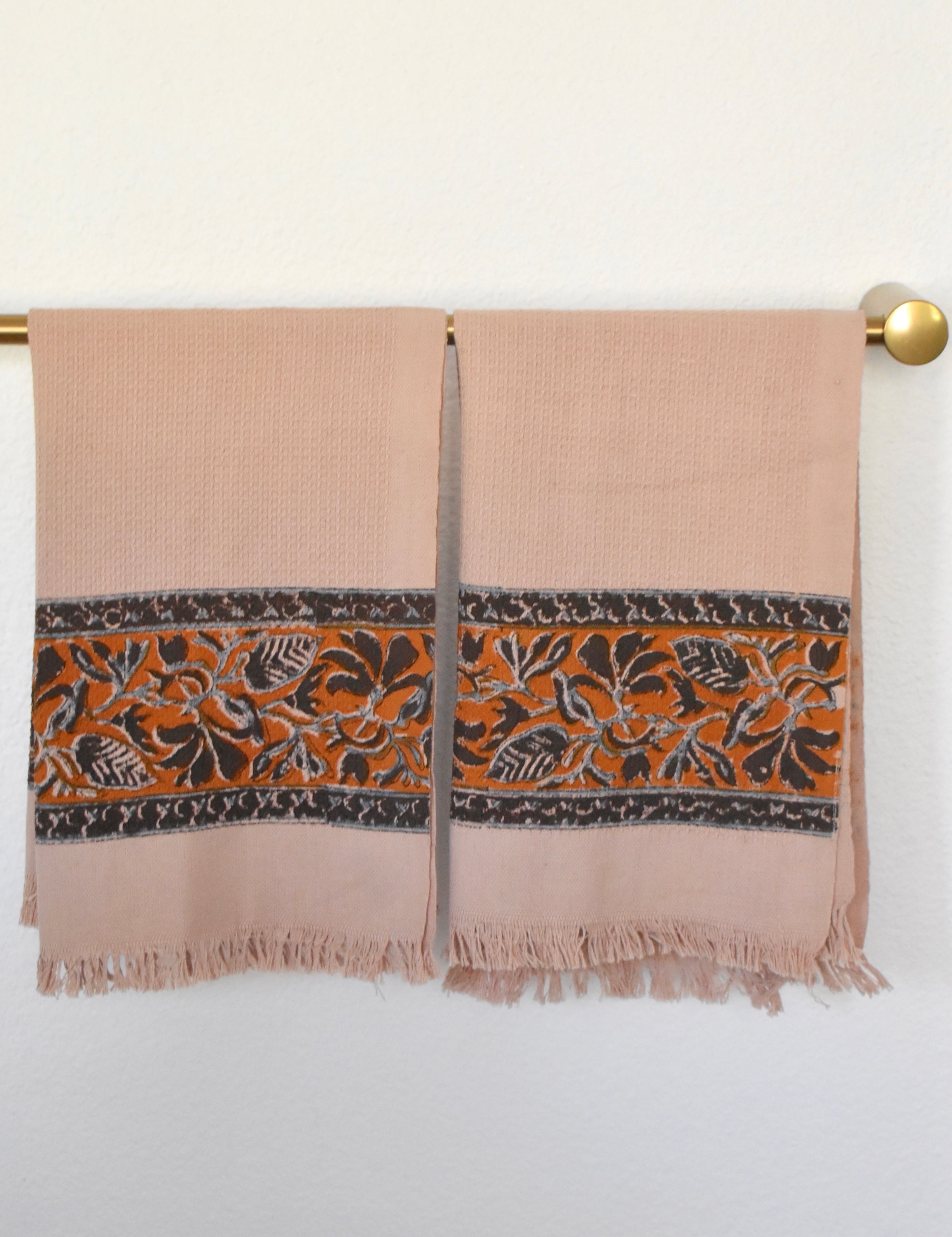 Block printed Cocoa khadi hand towels, hanging on a golden rod. Towels have a floral border print.