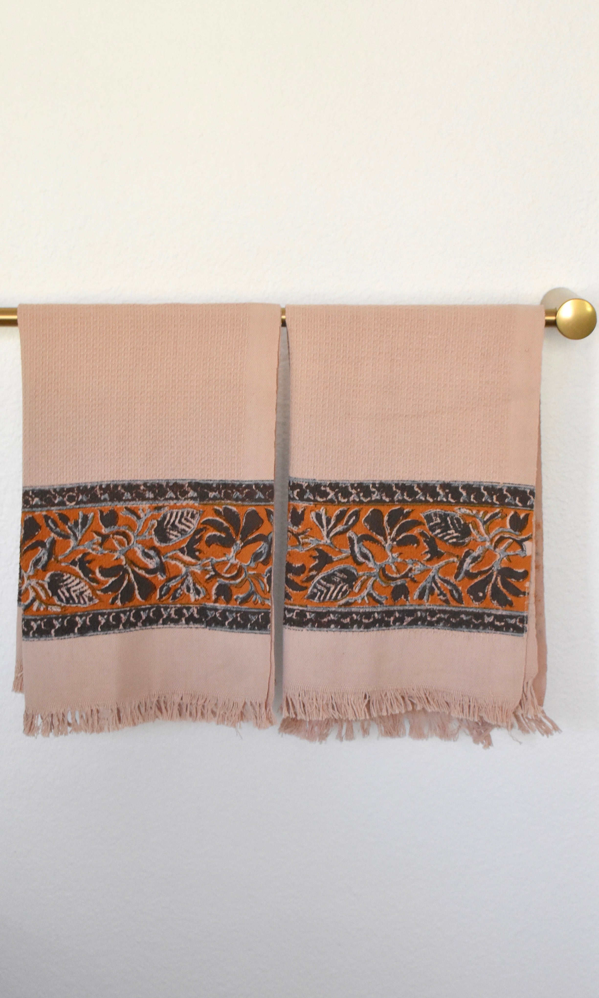 Block printed Cocoa khadi hand towels, hanging on a golden rod. Towels have a floral border print.