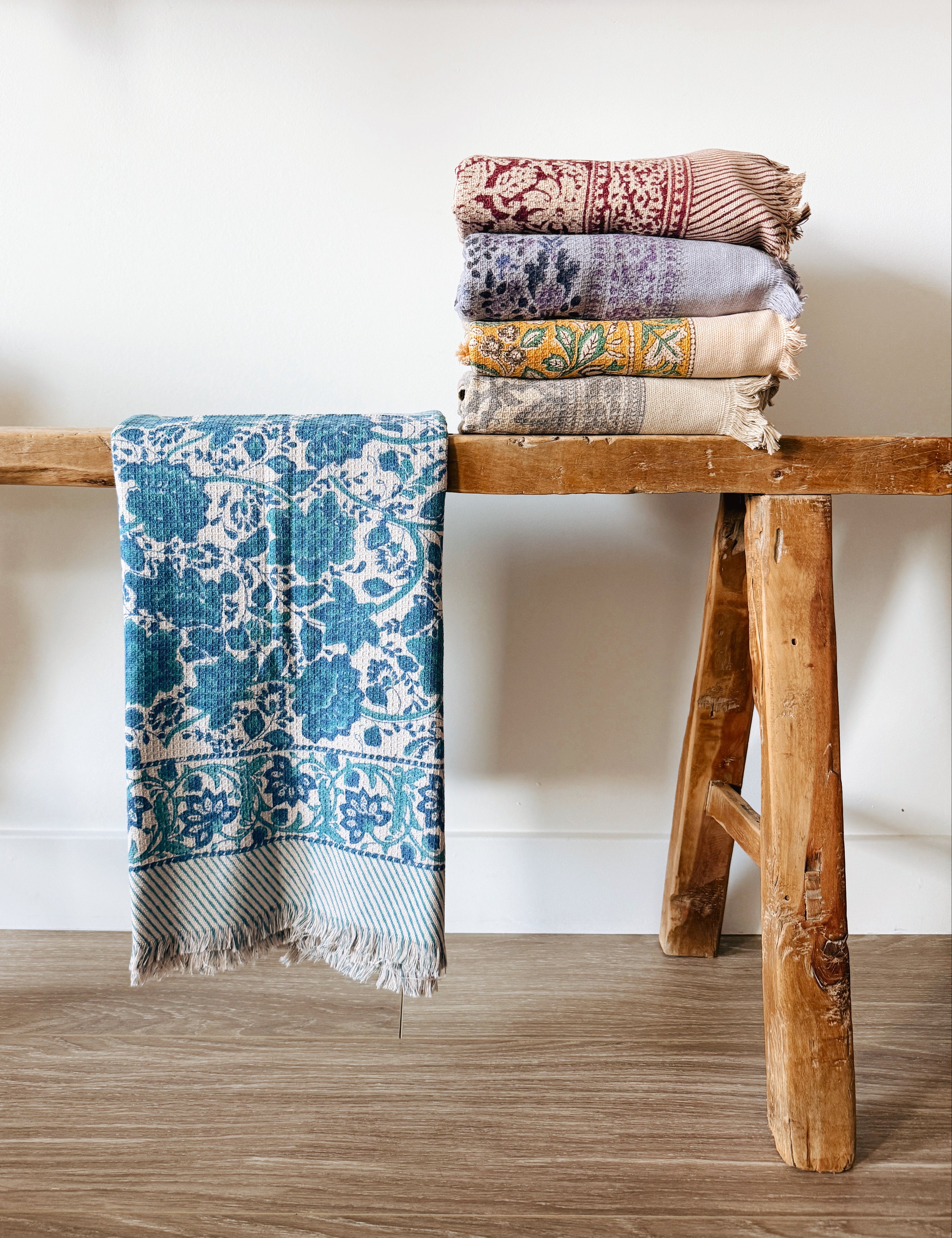 Stack of floral block patterned towels on a wooden stool against a white wall
