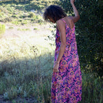 Back shot of woman wearing pink and purple floral printed strappy maxi dress, standing in nature