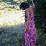 Back shot of woman wearing pink and purple floral printed strappy maxi dress, standing in nature